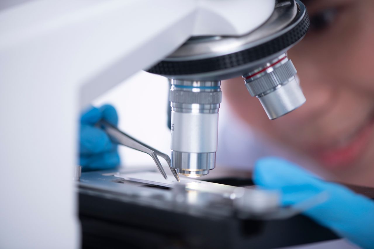 contact-bg Blurred unrecognizable person placing sample on microscope while making research during work in modern laboratory