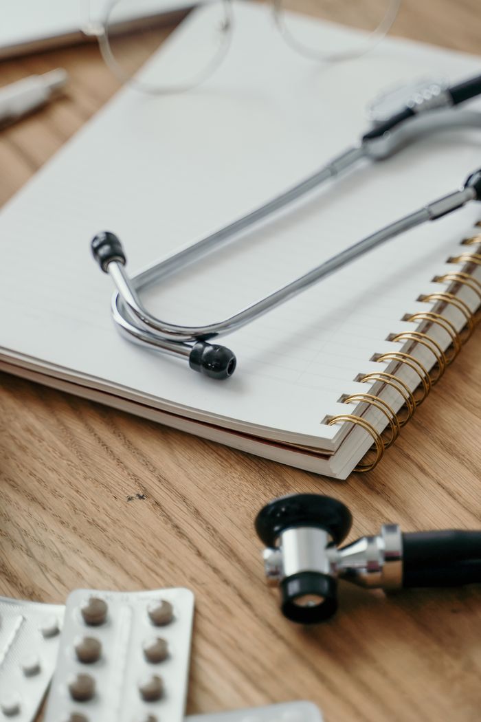 who-we-are Close-up of a stethoscope placed over a notebook with pills nearby, symbolizing healthcare themes.